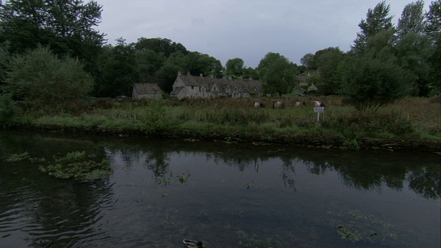 在英国格洛斯特郡的Bibury，石头小屋沿着一条平静的、树木繁茂的科林河排列。高清。视频素材