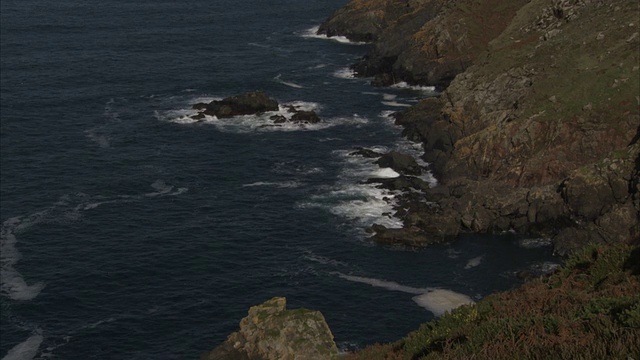 海浪冲击着岩石建筑附近的多岩石的海岸线。高清。视频素材