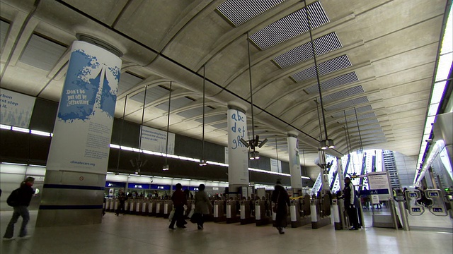 伦敦金丝雀码头地铁站(Canary Wharf Tube Station)的一根柱子上有一则广告，通勤者在这里进出检票口。高清。视频素材