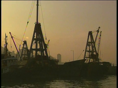 浅橙色的夜空映衬下，港口里摇摆的吊车的剪影视频素材