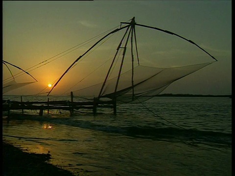 中国渔网的剪影，背景是夕阳，海浪轻轻拍打着喀拉拉邦的前景。视频素材