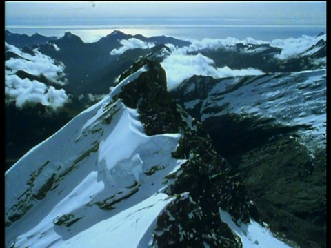 飞过白雪覆盖的山脉，在云的水平与令人惊叹的蓝天背景;南岛视频素材