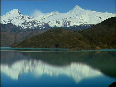 潘沿着广阔平静的湖泊离开了，巴塔哥尼亚的背后是白雪覆盖的山脉视频素材