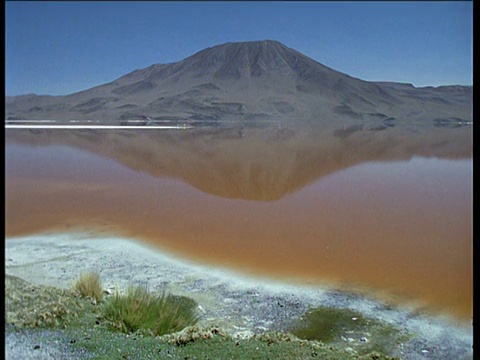 在蓝色天空下的休眠火山反射在橙色苏打湖，玻利维亚视频素材