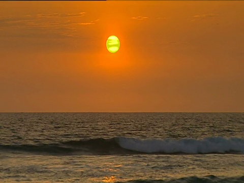 太阳在橙色的天空之上，在夕阳的温柔翻滚的波浪。视频素材