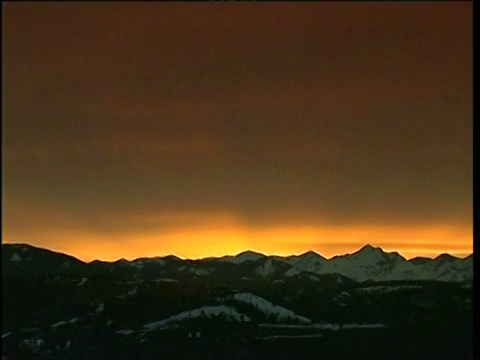 红色沙漠山脉的剪影放大到明亮的橙色日落天空上方的雪山视频素材