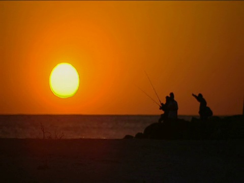 一群人在佛罗里达海滩上的橙色夕阳下钓鱼视频素材