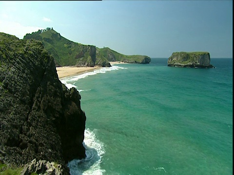 碧绿的海水缓缓地涌向沙滩，海浪拍打着崎岖的悬崖视频素材