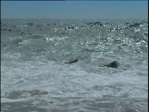 浪花拍打着海岸的岩石，海水在阳光下闪闪发光视频素材