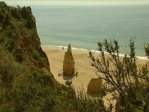 在沙滩中，人们站在岩石旁，海浪拍打着海岸视频素材