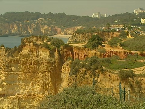 潘文石从多岩石的海岸线走到沙滩上的岩层，背景是沿着蓝色海洋行走的人们视频素材