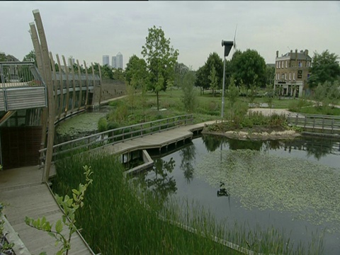 风力涡轮机旁边的池塘，在城市公园金丝雀码头建筑的背景里，英里结束公园伦敦视频素材