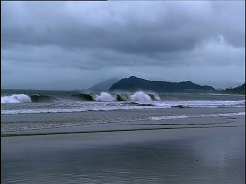 海浪在空荡的海滩上破碎，乌云密布的天空覆盖在婆罗洲的背景山视频素材