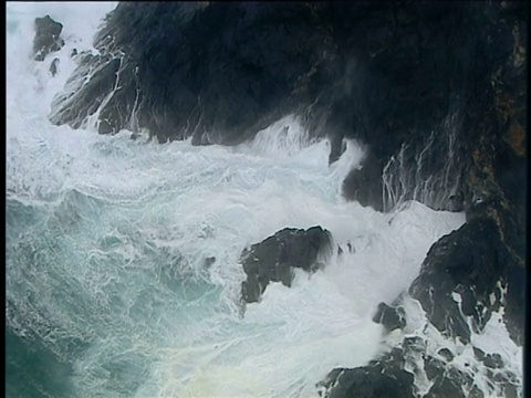 冒着泡沫的海浪在康沃尔悬崖底部汹涌撞击岩石视频素材