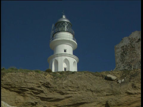 沙丘上的花和草，岩石上的波浪和白色的灯塔，映衬着Costa de la Luz深蓝色的天空视频素材