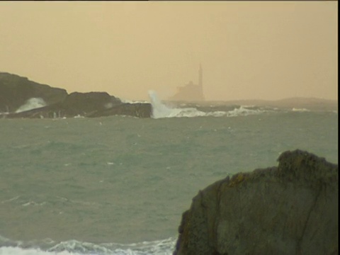 海浪冲击着海岸岩石灯塔在远处苏格兰视频素材