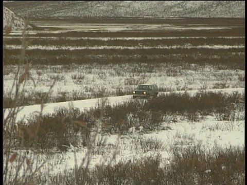 从积雪覆盖的山脉向下倾斜，沿着阿拉斯加下面的道路驾驶4x4视频素材