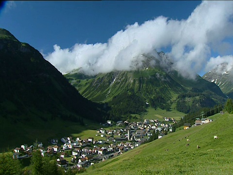 在奥地利下面的山谷中，山顶上的村庄聚集着蓬松的白云视频素材