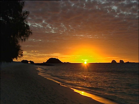 波浪轻轻拍打着沙滩，橙色的夕阳和鲭鱼天空映衬着马达加斯加的轮廓视频素材