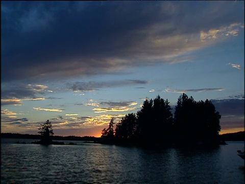 夕阳下的波光粼粼的湖树在前景的剪影映衬下的橙色辉光的地平线:明尼苏达州视频素材