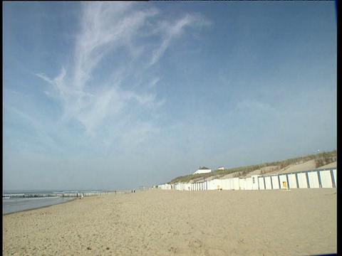 宁静的海滩景色，海浪轻轻翻滚，海滩上的小屋在左边，在右边;荷兰。视频素材