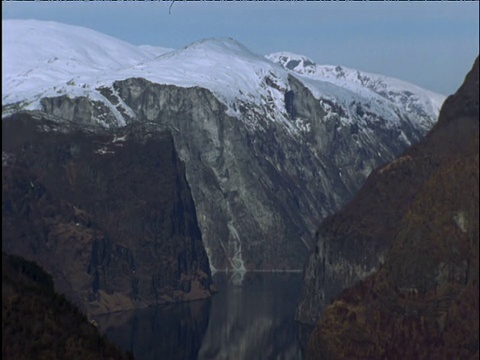 从积雪覆盖的山上向下倾斜到黑暗的峡湾水域视频素材