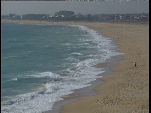 轻柔的海浪拍打着宽阔的沙滩，远处的Costa De La Luz有建筑物视频素材