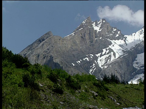 潘正穿过岩石山峰和斑驳的雪绿色斜坡，树在前景瑞士视频素材