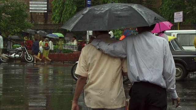 行人撑着雨伞在下雨的街道上行走。高清。视频素材