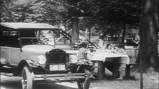 1910年代的人们在公园的餐桌上野餐，在操场旁/在前景/纪录片中视频素材