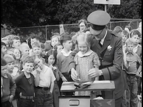 1936年，警察在桌子旁为小女孩指纹/背景中的一群孩子/新闻短片视频素材