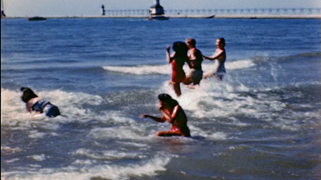 20世纪40年代，2个男人+ 4个穿着泳衣的女人在海滩上跑进水里视频素材