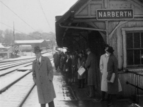 1955年，戴着帽子和外套的男男女女在白雪覆盖的站台上等着“NARBERTH”标志视频素材