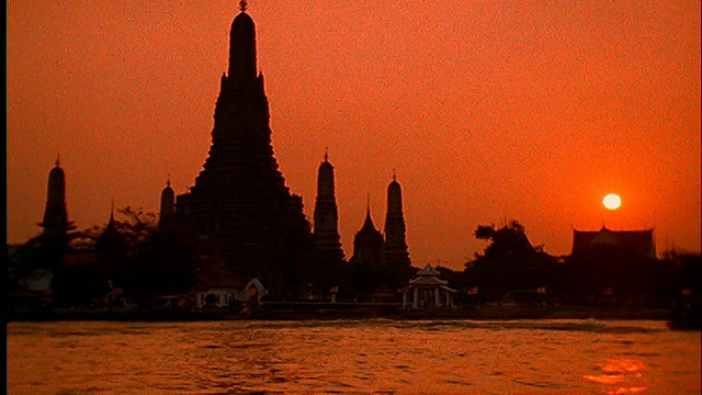 慢镜头显示湄南河上的佛教寺庙(Wat Arun)和船只的剪影/日落/曼谷视频素材