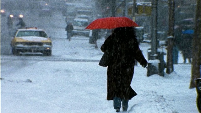 在暴风雪/纽约，一名女子撑着红伞走在城市街道上视频素材