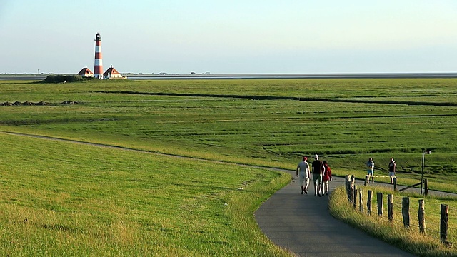 在德国石勒苏益格荷尔斯泰因州，北弗里斯兰瓦登海/ Westerhever，人们穿过绿地走向Westerhever灯塔视频素材