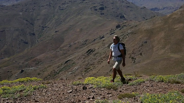 徒步旅行者穿过草地俯瞰高山，然后下山视频素材