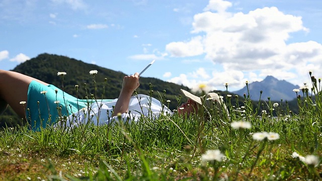 机架焦点的女人放松在山区草地，使用数字平板电脑视频素材