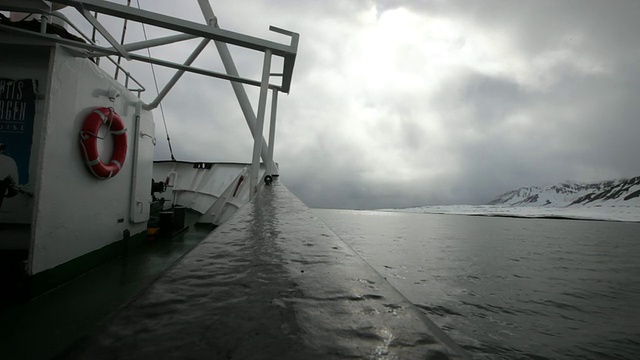 在伊斯峡湾、斯匹次卑尔根群岛、斯瓦尔巴特群岛上，沿着被雪覆盖的山脉航行的小船;暴风雨天气和多云的天空视频素材