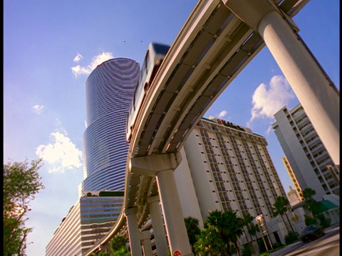 低角度的单轨电车在街道交通上方的地铁轨道上行驶/ Centrust Tower背景/迈阿密视频素材