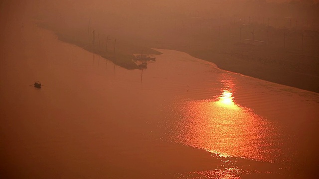 粉红色的夕阳洒在宽阔的河面上，远处的河岸和孤零零的小船映入眼帘。印度视频素材