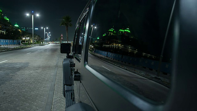 黑色的公路汽车在夜间通过朱美拉棕榈岛隧道，上棕榈岛返回迪拜城。汽车的一边在前景。车身表面和背景上的条纹反射。视频素材