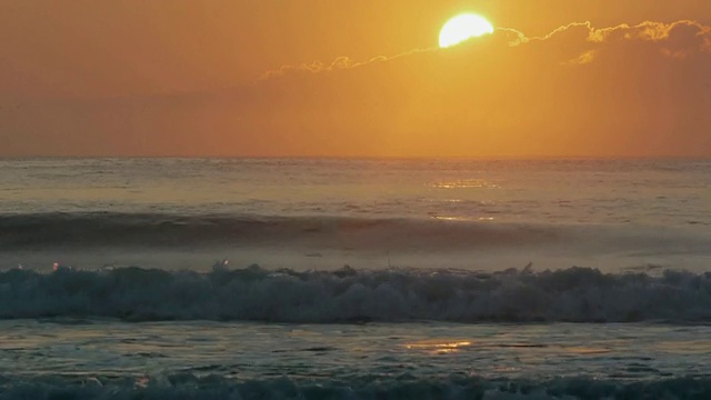 橙色的太阳从大西洋上空的云彩后面升起，波浪打破前景，科德角国家海岸，马萨诸塞州视频素材