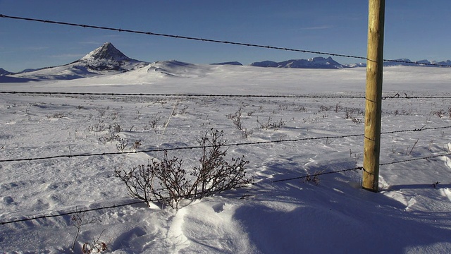 POV潘向左，然后向右的乡村道路和铁丝网围栏上的雪堆覆盖草原，背景是山脉。视频素材