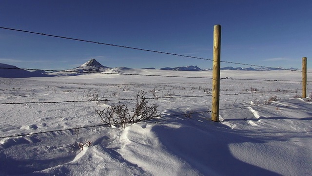 POV潘右然后左到乡村公路和铁丝网围栏上的雪堆覆盖草原与背景的山脉。视频素材