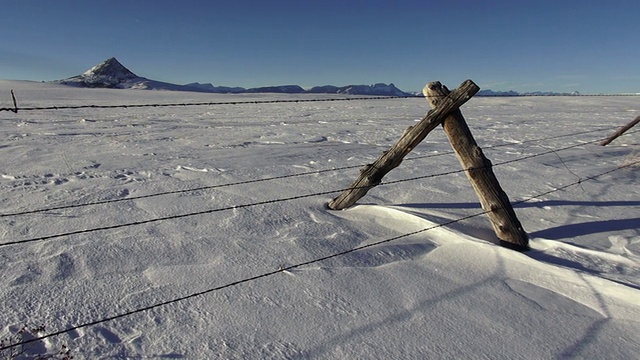 潘右坡的铁丝网上覆盖着雪堆，草原景观以群山为背景。视频素材