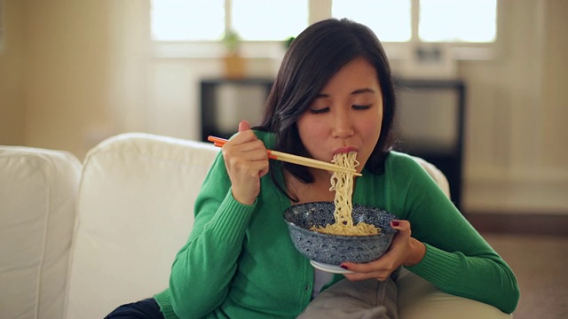 年轻女子在家里吃面条，看着镜头。视频素材