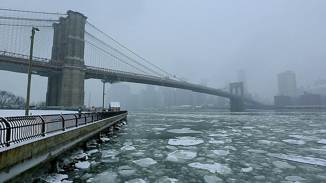 在布鲁克林大桥公园的大雪中，摄像机捕捉到了曼哈顿摩天大楼和覆盖东河的移动浮冰。从后面可以看到朦胧的布鲁克林大桥和曼哈顿摩天大楼的雪景。视频素材