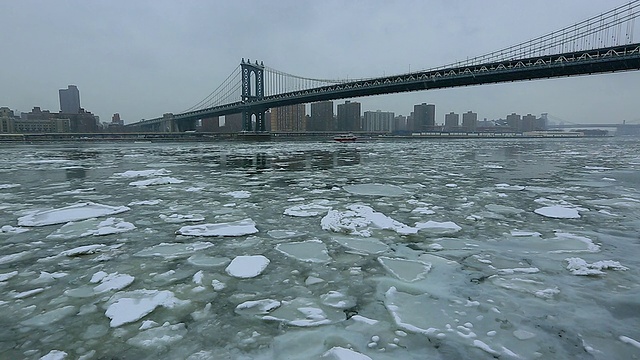 摄像机捕捉到了下雪期间覆盖东河的流动浮冰。船在雪中穿过朦胧的曼哈顿大桥。从后面可以看到曼哈顿下城的住宅。视频素材