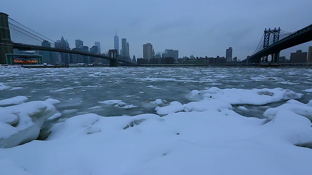 PAN摄像机捕捉到了下雪期间覆盖在布鲁克林大桥和曼哈顿大桥之间的东河上移动的浮冰。从后面可以看到朦胧的布鲁克林大桥和曼哈顿摩天大楼的雪景。视频素材